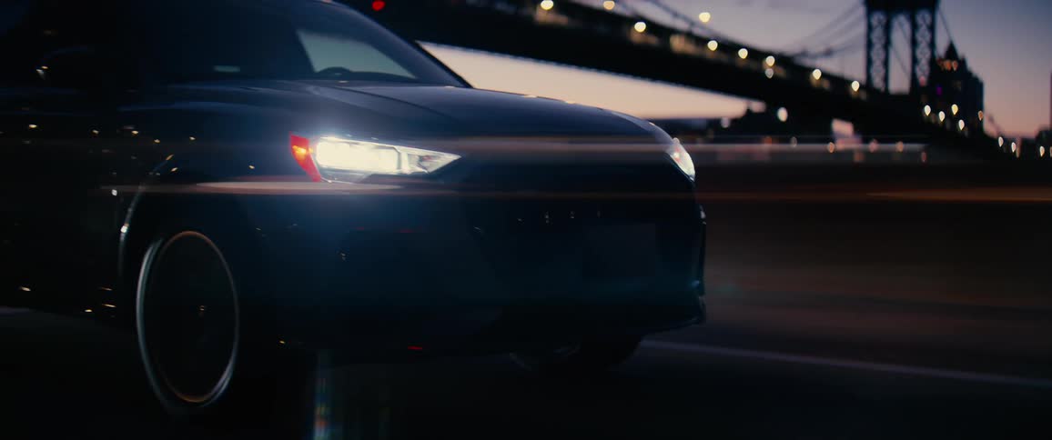 Vehicle with headlights on traveling on a highway with a bridge in the background