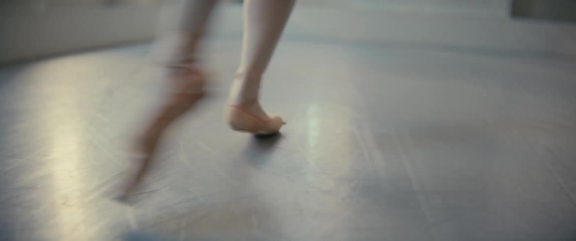 A closeup of a ballet dancers feet in pointe shoes performing ballet poses on a studio floor