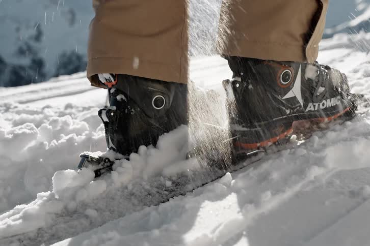 A person secures ski boots to skis while standing in the snow on a bright sunny day
