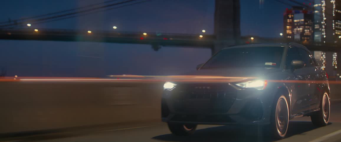 A sleek white suv driving at night on a city highway with a blurred motion effect illuminated by streetlights and the glowing skyline with a bridge visible in the background