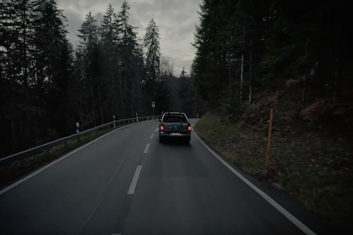 A dark gray volkswagen amarok pickup truck drives on a winding road through a dense forest