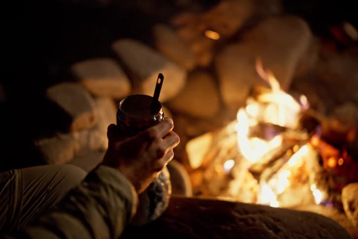 Pair of hands pouring water into a glass in front of a campfire at night