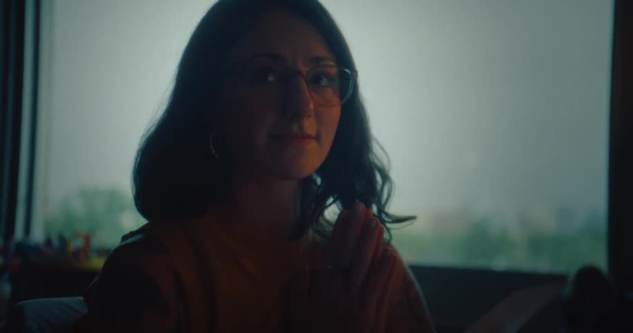 Woman sitting in a room with her hands clasped together