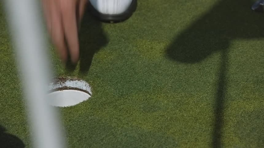 A person sinks a golf ball and then takes it out of the hole