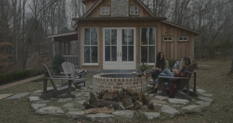 Two girls sit in chairs with mugs conversing outside
