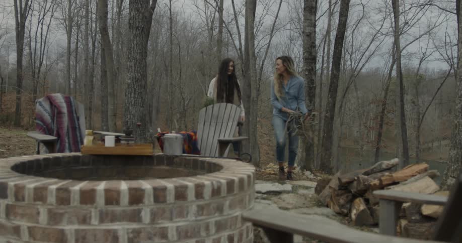 Two women bring over supplies for a campfire