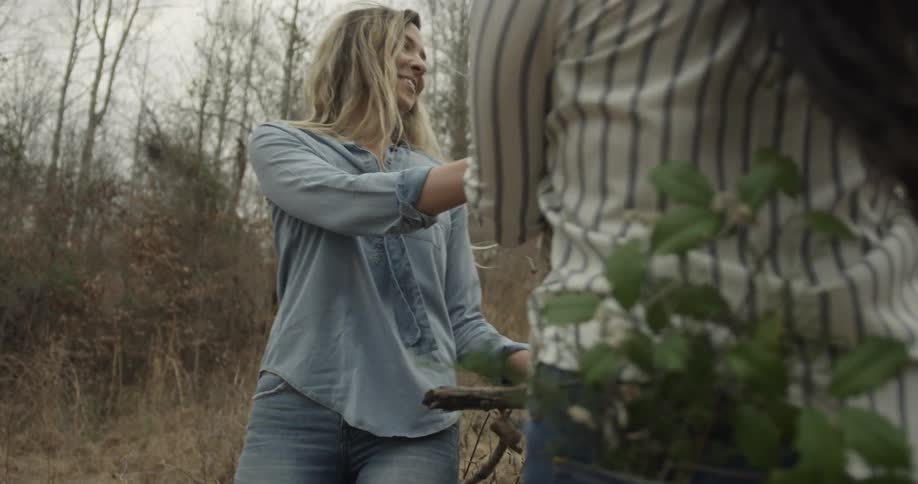 Two women carrying sticks run in the woods