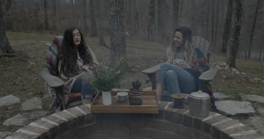 Two women chat around an outdoor fire on a chilly day
