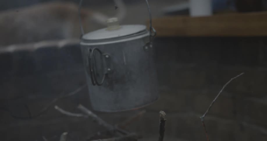 A metal pail hangs over a campfire