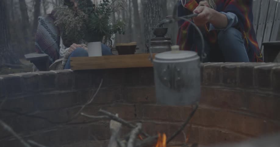 A person is warming a kettle over a campfire
