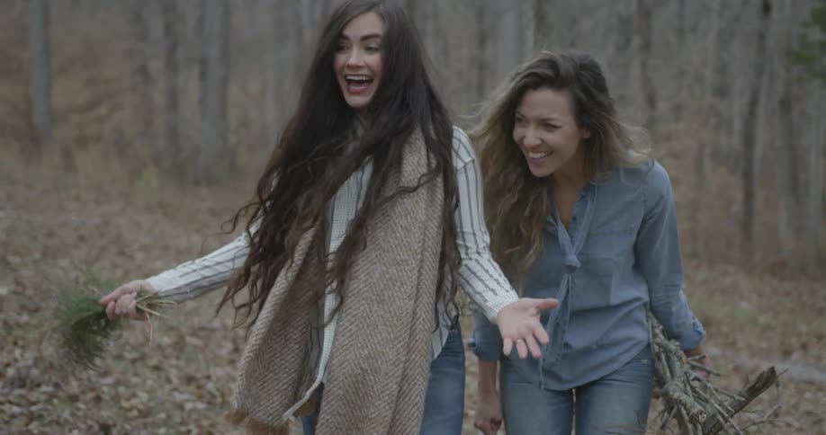 Two women laugh while carrying flowers and sticks