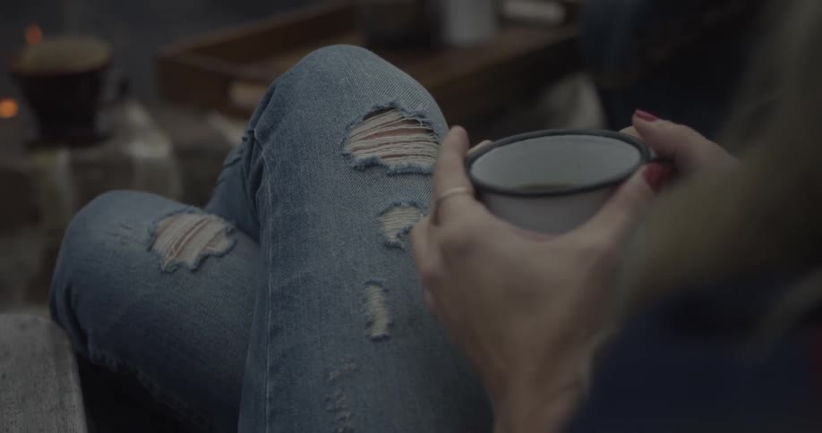 Woman holding a coffee cup with her legs crossed wearing stylish jeans with holes in them