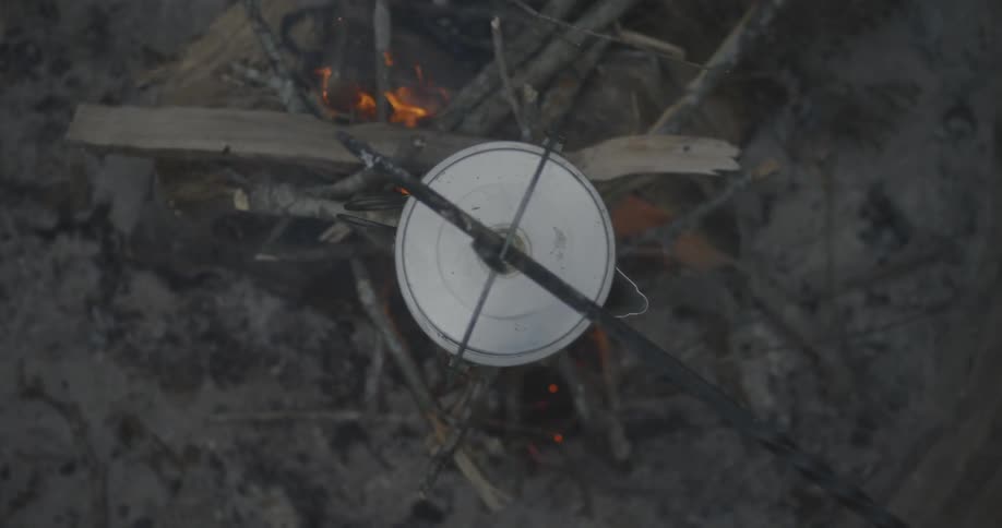 A metal kettle hangs over a campfire