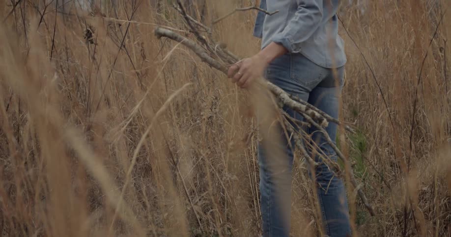 A woman carries sticks and flowers in a field