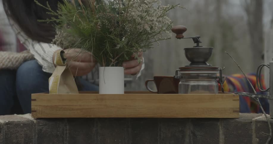 A woman places and arranges branches in a mug
