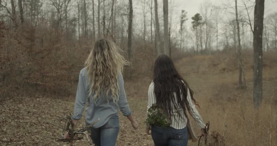 Two women carrying sticks walk in the woods
