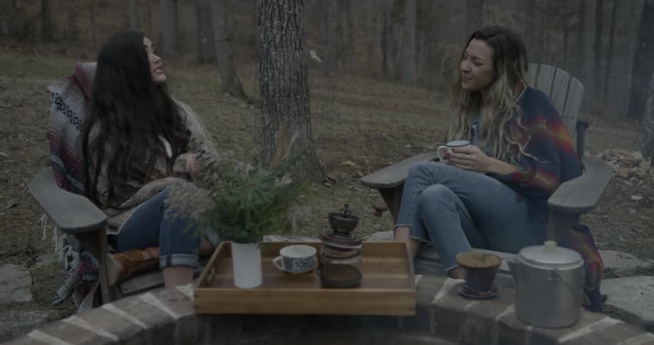 Two women talk in front of a fire pit
