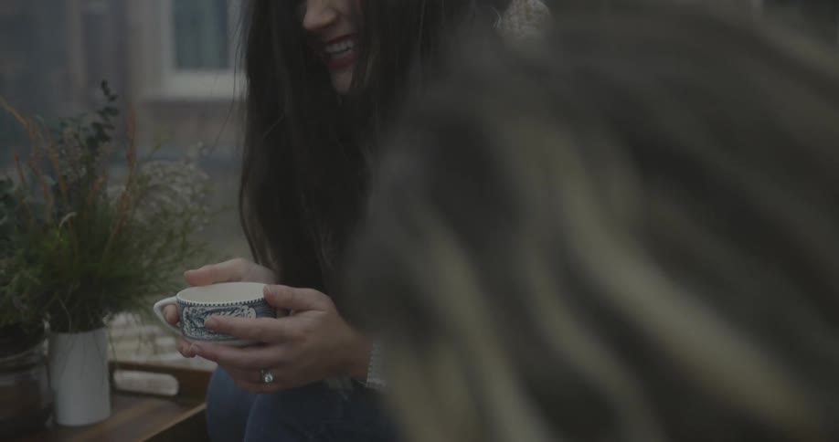 Two women laugh while drinking hot beverages outside