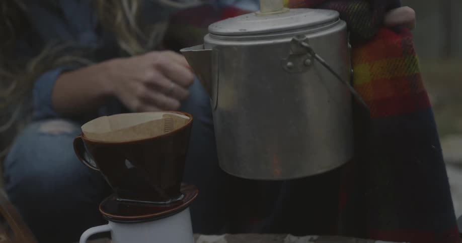 A woman lifts a metal kettle to pour over coffee in a filter