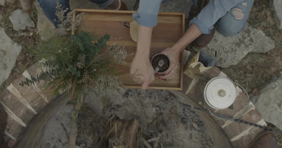 Coffee is poured into a grinder next to an outdoor fire pit