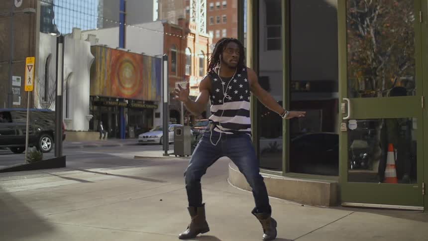 A man is performing a dance on a city sidewalk during the day