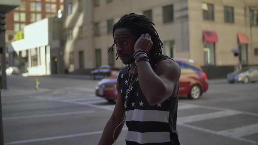 A man has his hand up to his ear as he is walking in the city
