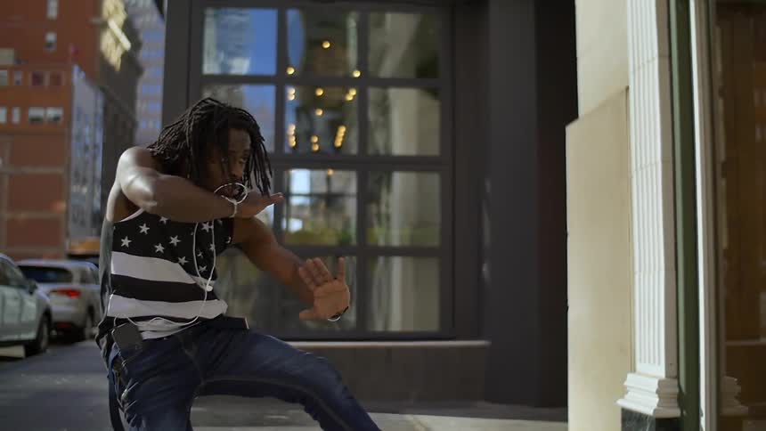 A man is dancing on the sidewalk near a building