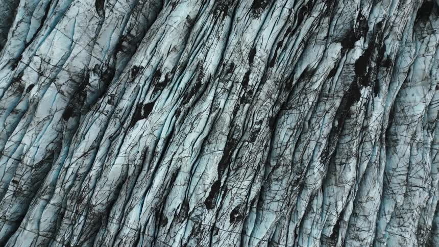 A view of a glaciers surface characterized by blue ice with numerous dark streaks and crevices