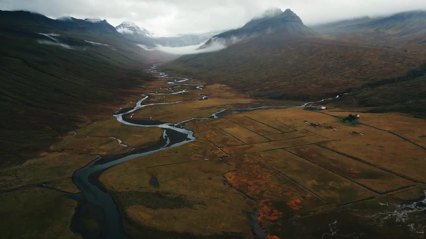 Aerial shot of a winding river surrounded by snowy mountains
