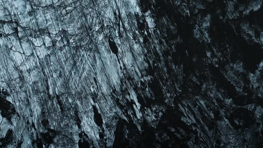 A closeup of a textured surface with one half predominantly light gray and the other half a deep dark gray almost black with marks and estriations