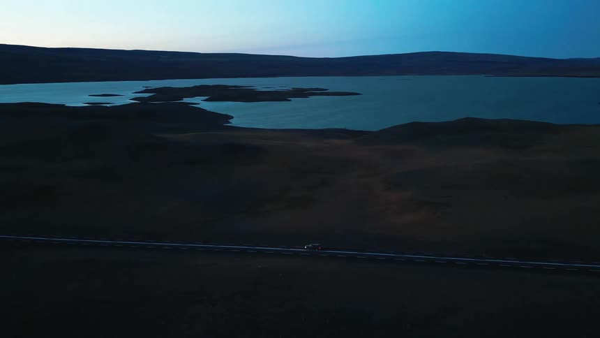 Aerial panorama of a highway with a vehicle traveling alone and in the background a lake and the silhouette of mountains