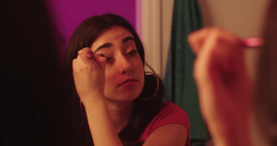 The face of a young girl who is looking at herself in the mirror while putting on makeup on her eyes