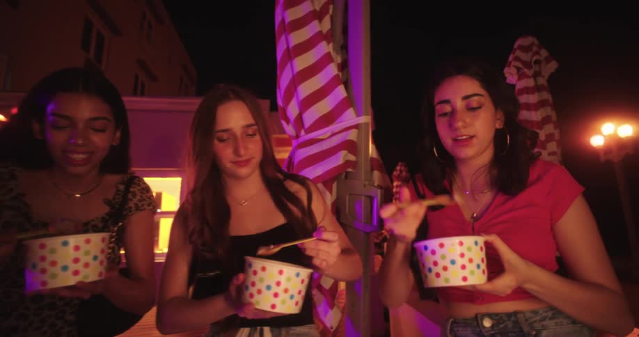 Three women outdoors at night eating ice cream