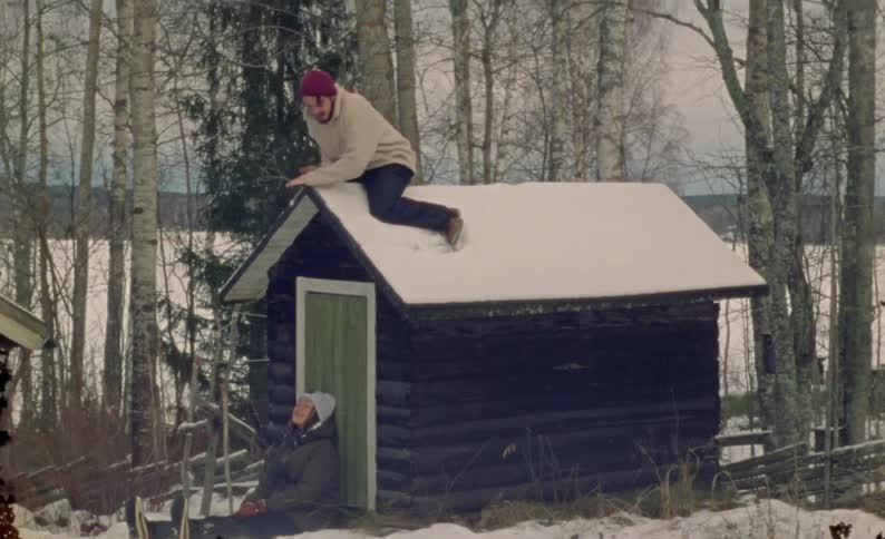 Man climbing out of a cabin and running in the snow with a woman behind him