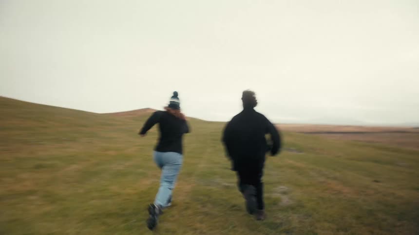 Man and woman running across a large grass field on a cloudy day
