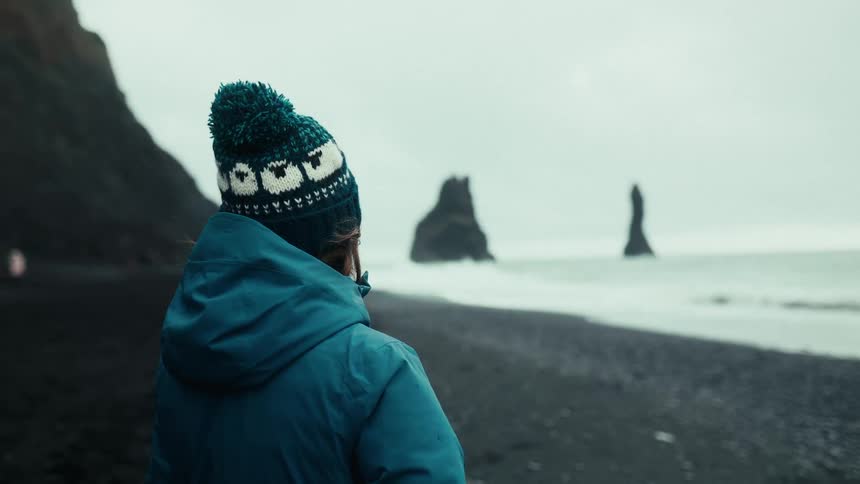 Person wearing a hat and a blue jacket enjoying the view of a sea in winter