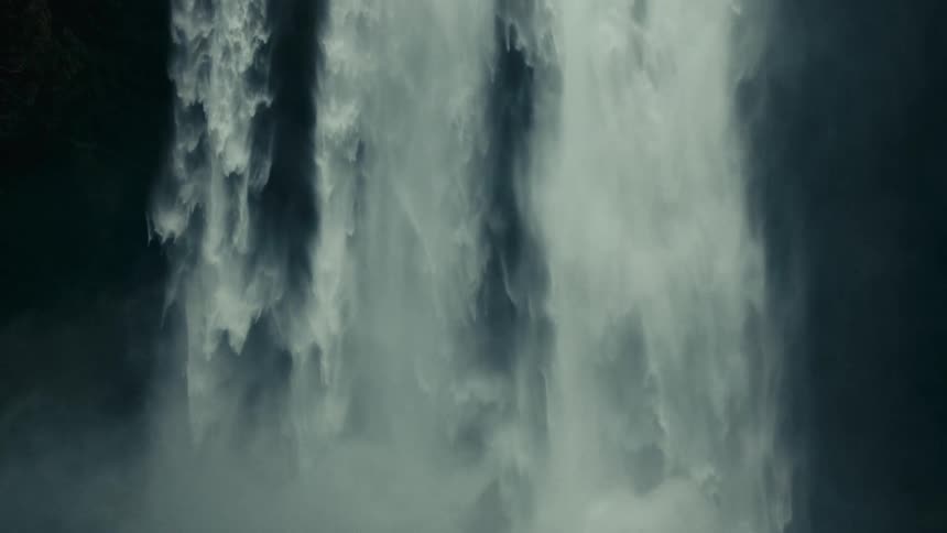 A camera pans down a powerful waterfall showcasing the cascading water as it plunges towards the pool below