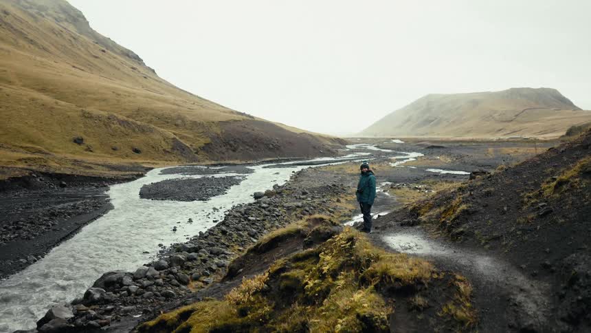 A woman stands near a glacier river in the mountains