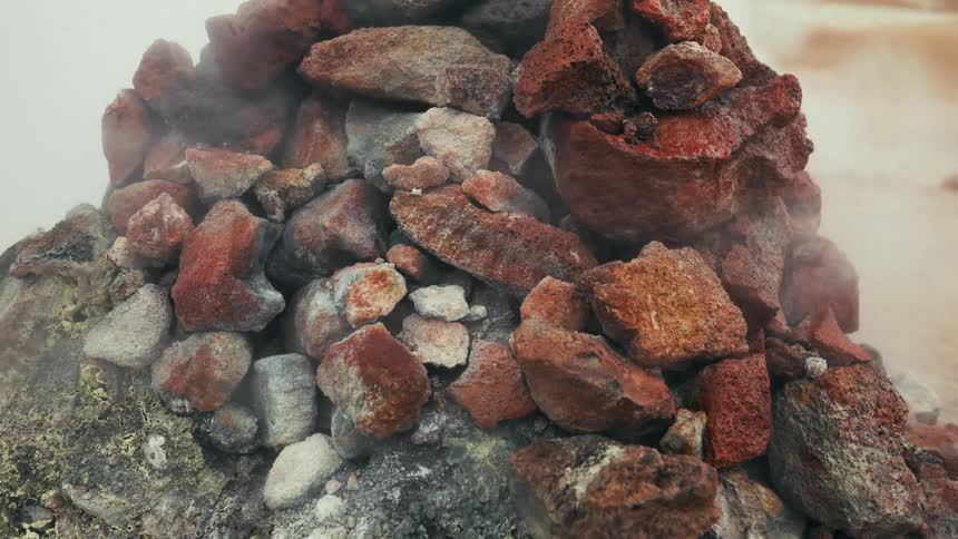 A pile of small stones with reddish colors and some smoke coming out