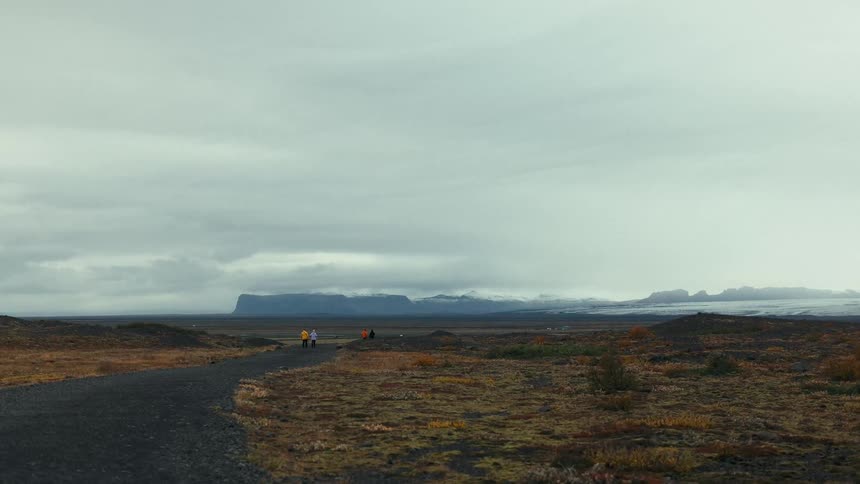 Four people walking through a landscape with a trail and mountains in the background