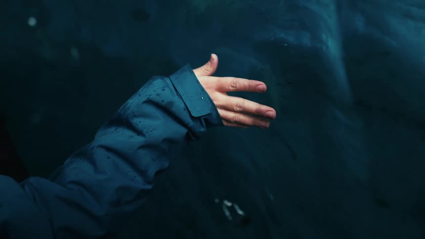 Female hand who is wearing a blue longsleeved outfit and he is running his hand over a blue glacier wall