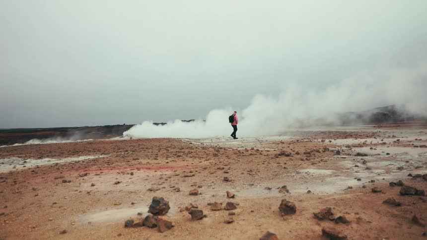 Person wearing a jacket and backpack walking in a natural area that emits steam