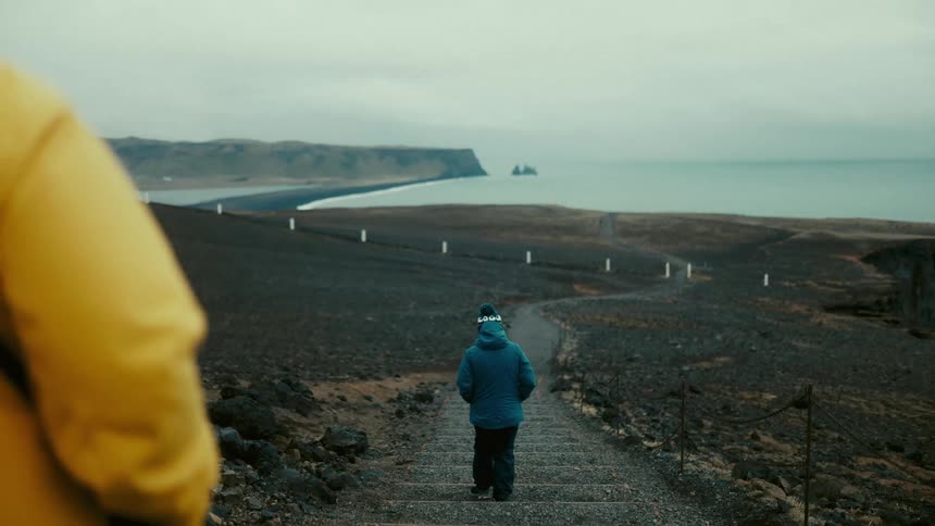 Two people walking down the stairs of a trail leading to the ocean in a winter region