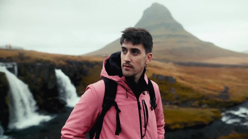 Man in a pink jacket enjoying the view at the edge of a waterfall with a towering mountain in the background