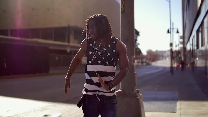 A man dances on a city sidewalk in the sunshine