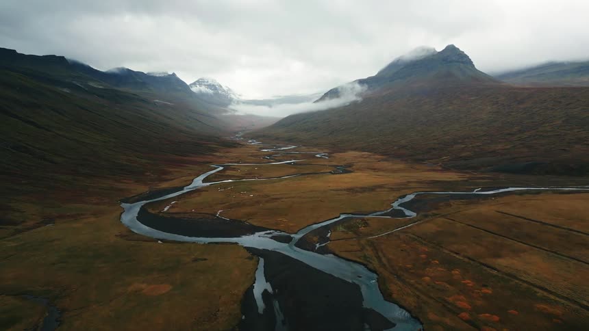 Aerial view of a winding river surrounded by mountains on a cloudy day