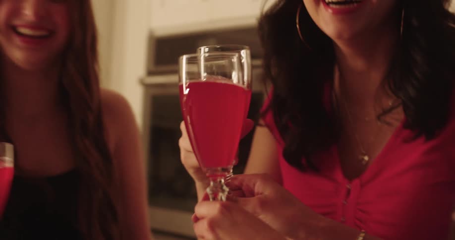 A group of teenage friends toasting with glasses filled with a red beverage in a kitchen