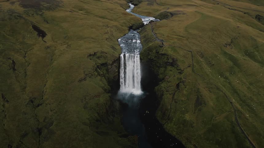 A small waterfall coming from a river in a region with low grass fields on the sides