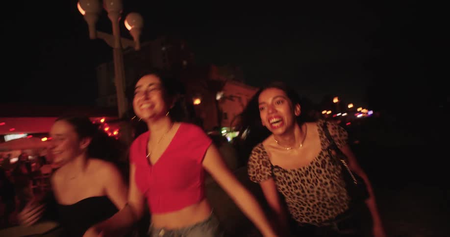 A group of teenage friends have fun running while holding hands during a night out in town