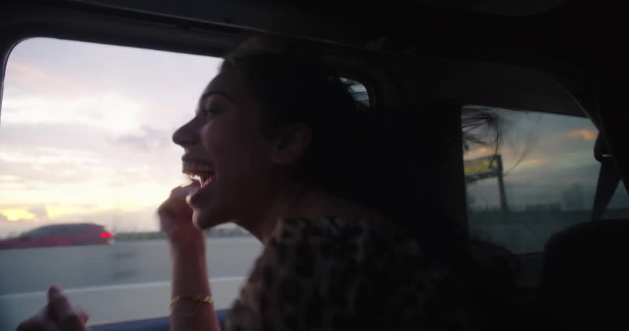 A girl is singing near the open window in a car her hair flowing in the wind having fun and enjoying the moment